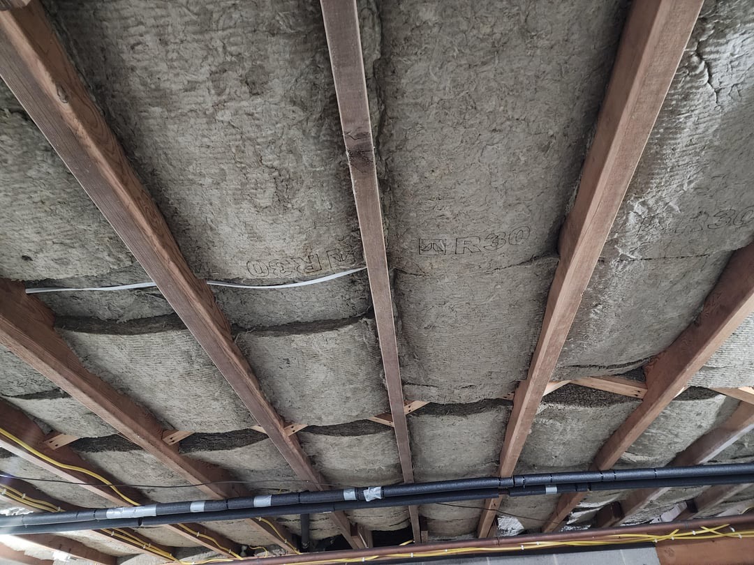 Insulation fitted between wooden floor joists above crawl space plumbing